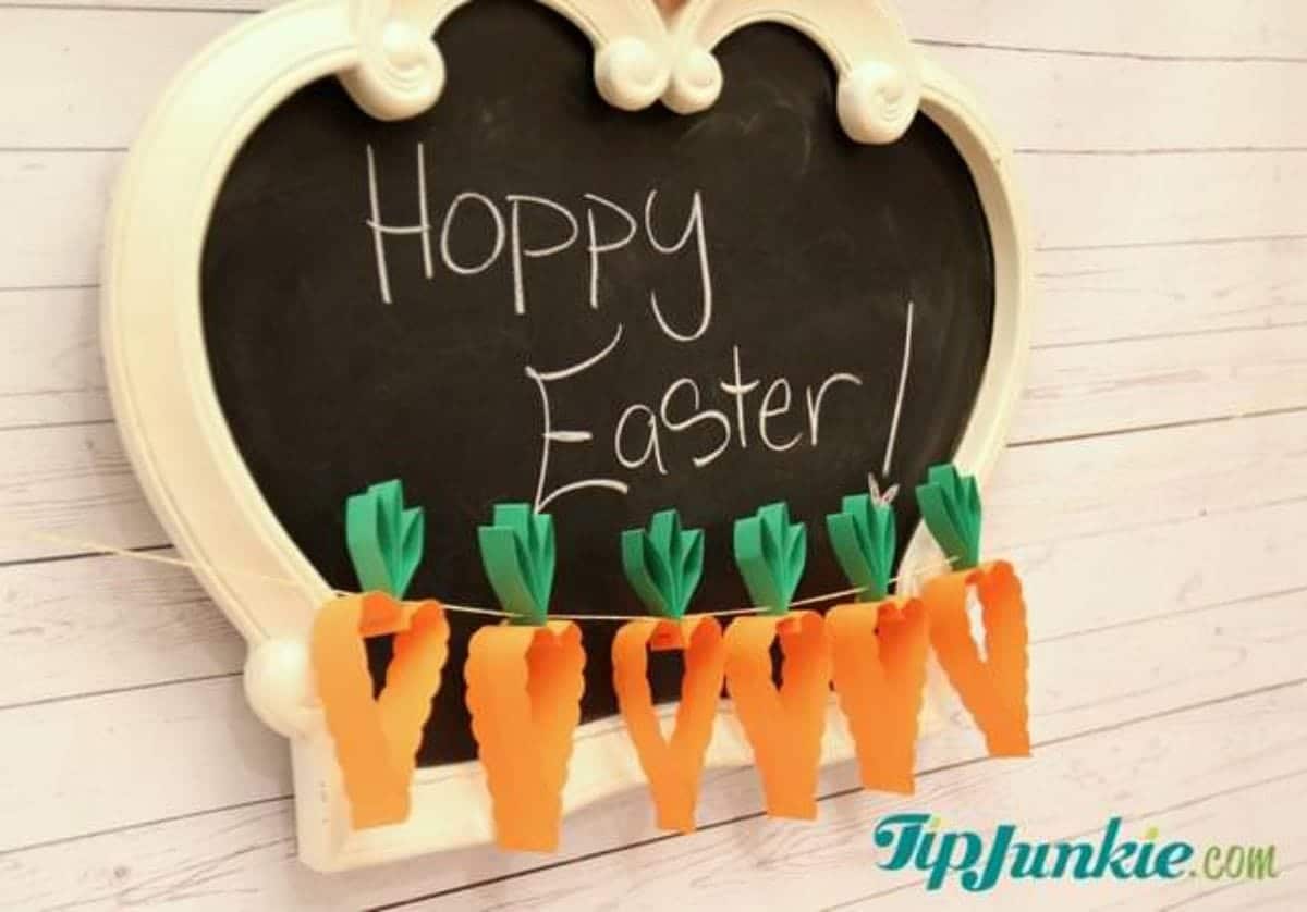 A blackboard with chalk writing saying "happy easter!" sits behind a garland of 3D paper carrots