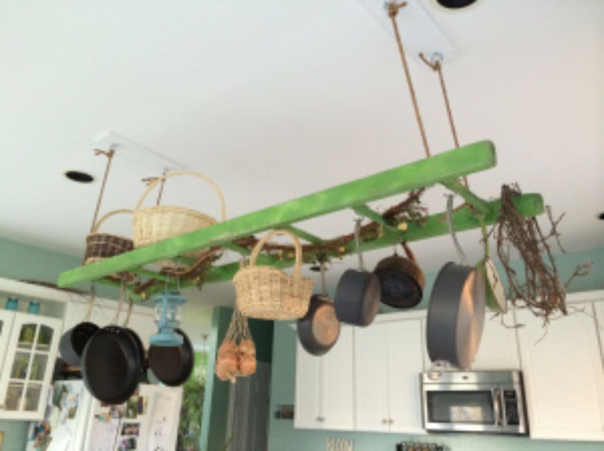 Hanging from a white ceiling with rope is a green ladder. Hanging from the ladder are several pots and pans